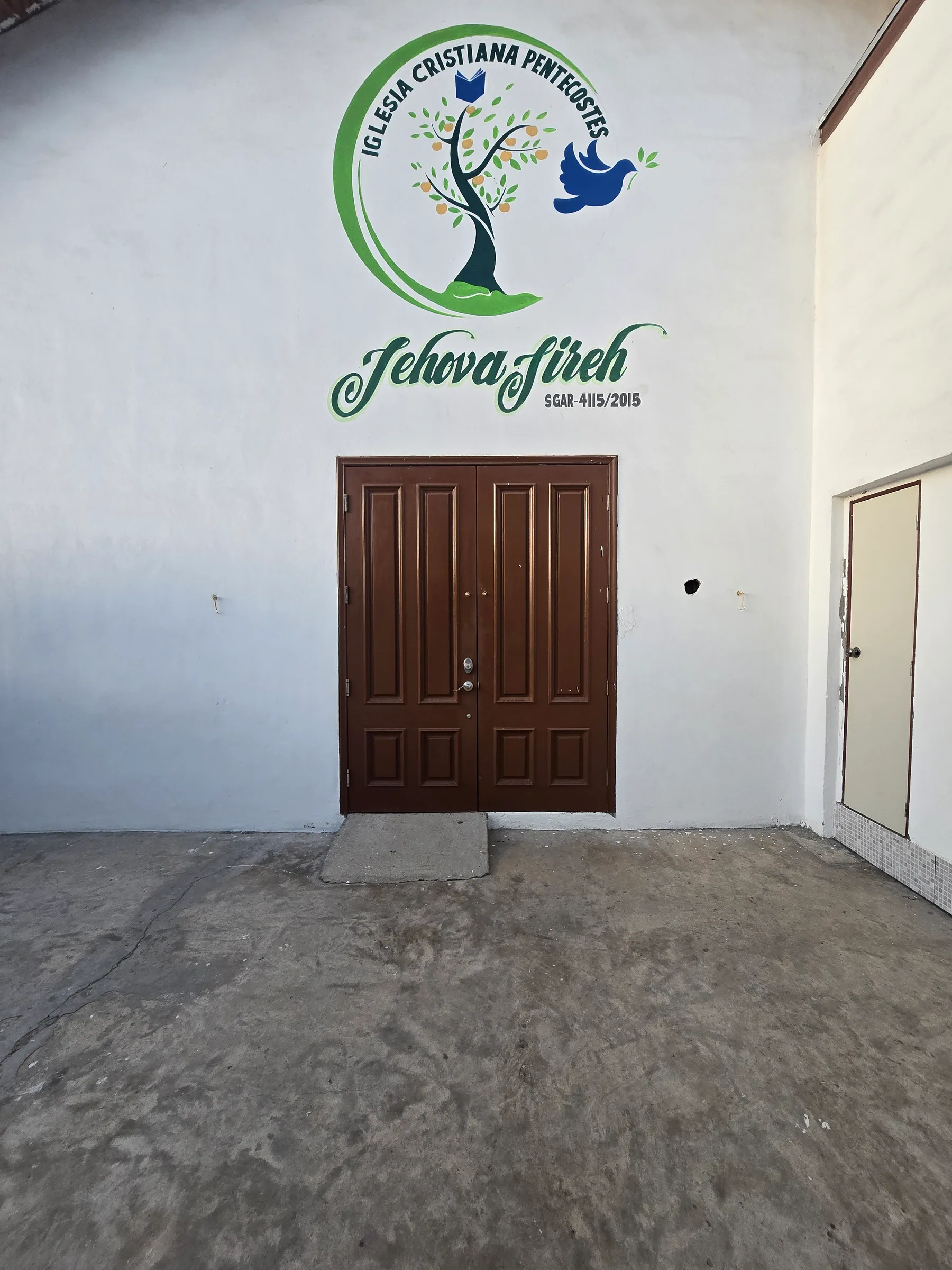 Entrada de Casa Jireh con puerta doble color madera y el logotipo visible sobre la fachada