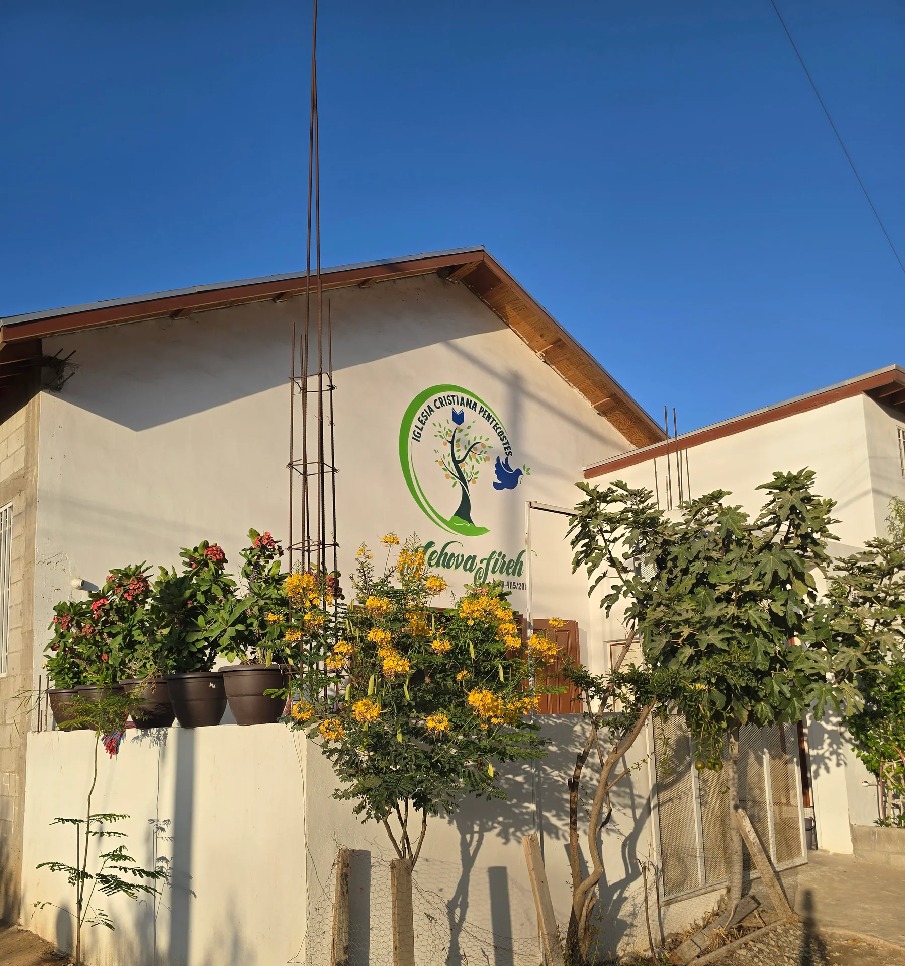 Vista de Casa Jireh desde la calle: fachada blanca con el logotipo, plantas al frente y acceso por el costado derecho