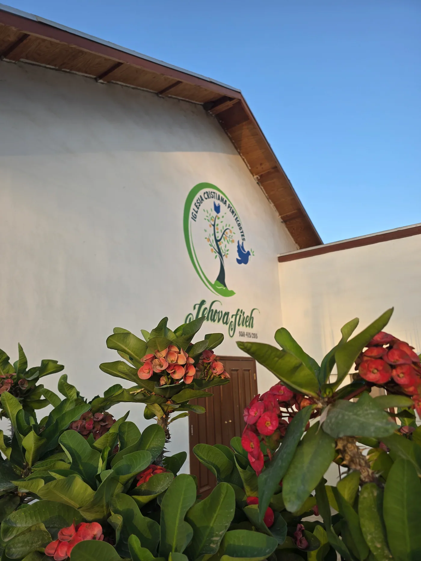 Plantas con flores frente a la entrada de Casa Jireh, con el logotipo visible sobre la fachada